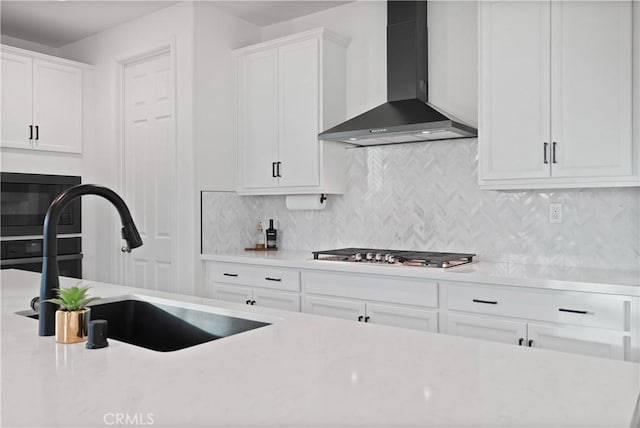 kitchen featuring stainless steel gas cooktop, wall chimney exhaust hood, sink, and white cabinetry