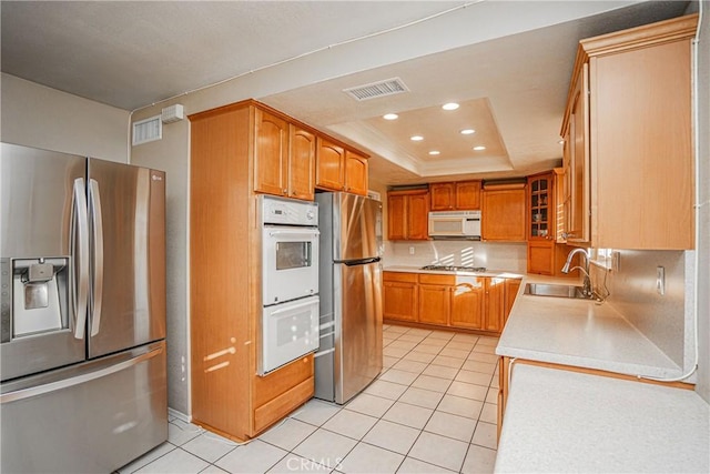 kitchen featuring light tile patterned floors, stainless steel appliances, tasteful backsplash, a tray ceiling, and sink