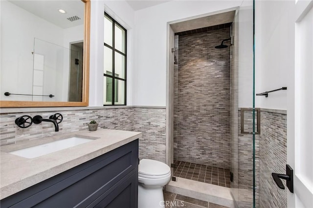 bathroom featuring toilet, vanity, tile walls, tile patterned flooring, and a shower with shower door