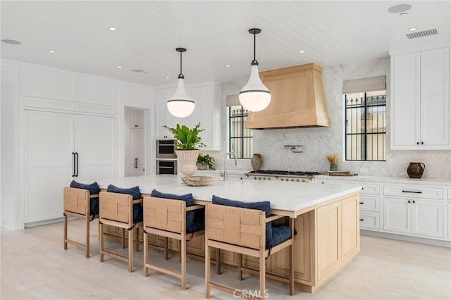 kitchen featuring premium range hood, a large island, decorative backsplash, hanging light fixtures, and white cabinets