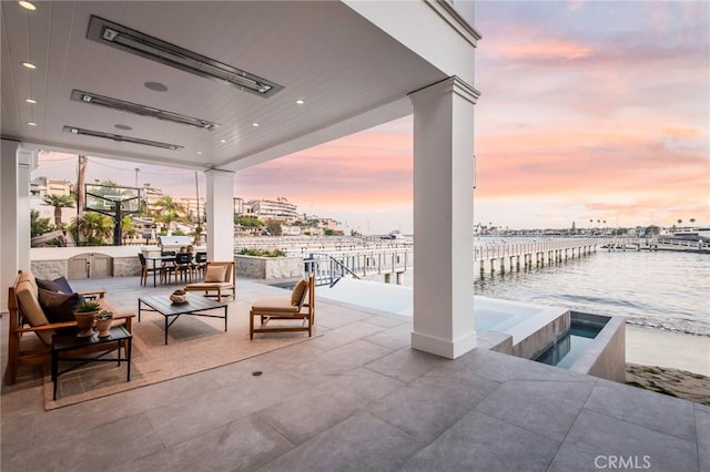 patio terrace at dusk featuring an in ground hot tub, an outdoor living space, and a water view