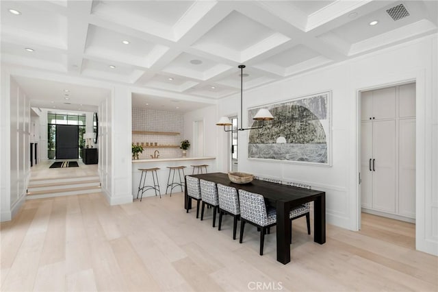 dining space with a chandelier, light wood-type flooring, beamed ceiling, and coffered ceiling