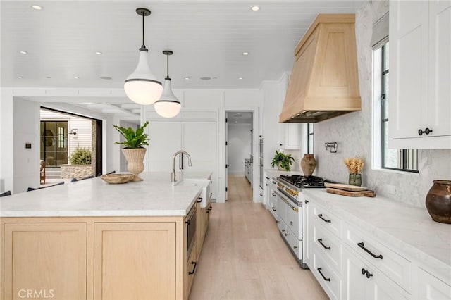 kitchen featuring light hardwood / wood-style floors, a center island with sink, a healthy amount of sunlight, hanging light fixtures, and custom range hood