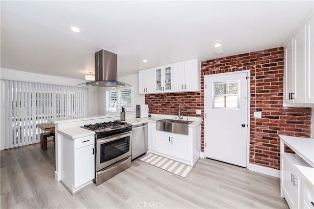 kitchen featuring island exhaust hood, stainless steel appliances, brick wall, white cabinets, and sink