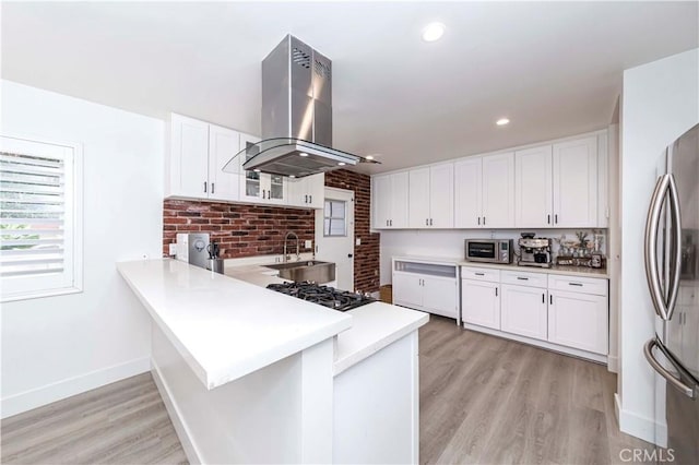 kitchen featuring kitchen peninsula, island exhaust hood, light wood-type flooring, stainless steel appliances, and white cabinets