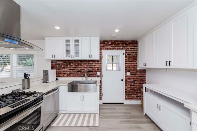 kitchen featuring brick wall, white cabinetry, wall chimney exhaust hood, and sink