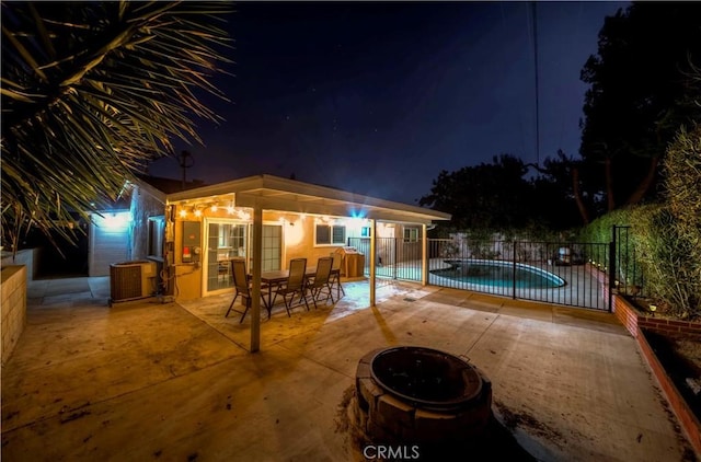 pool at night with a patio area and a fire pit