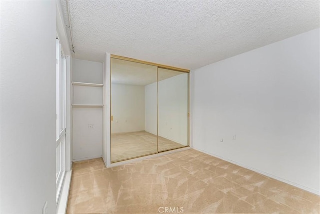 unfurnished bedroom featuring light carpet, a textured ceiling, and a closet