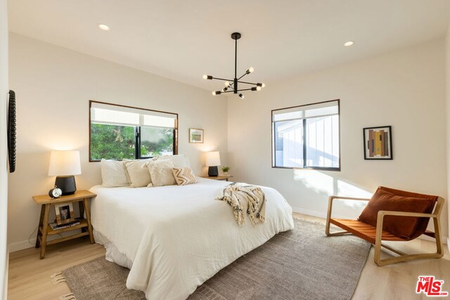 bedroom with multiple windows, light hardwood / wood-style floors, and an inviting chandelier