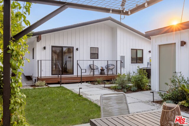 back house at dusk featuring a wooden deck and a lawn