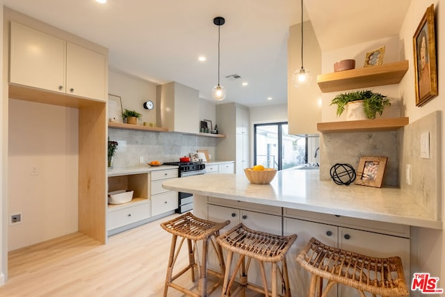 kitchen featuring white cabinetry, hanging light fixtures, stainless steel range with gas stovetop, tasteful backsplash, and kitchen peninsula