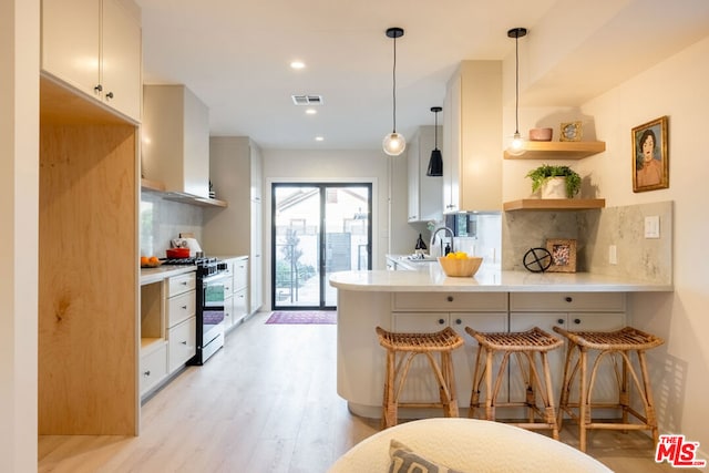 kitchen featuring a breakfast bar, stainless steel range with gas cooktop, kitchen peninsula, pendant lighting, and white cabinets