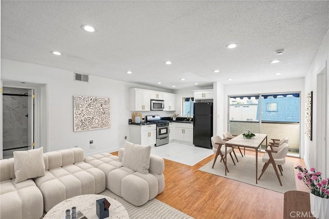 living room with a textured ceiling, visible vents, baseboards, light wood finished floors, and recessed lighting