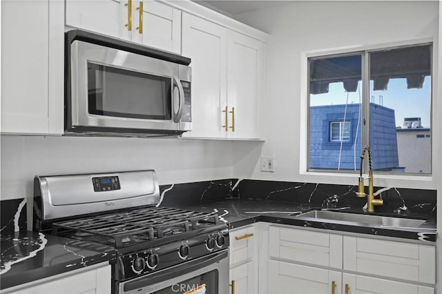 kitchen featuring stainless steel appliances, dark stone countertops, white cabinetry, and sink