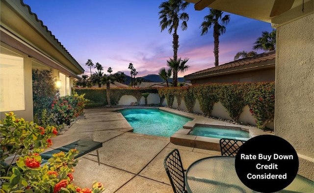 pool at dusk with an in ground hot tub and a patio area