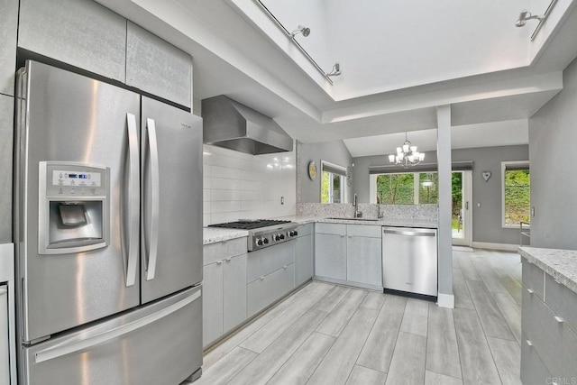 kitchen with stainless steel appliances, a notable chandelier, track lighting, wall chimney exhaust hood, and sink