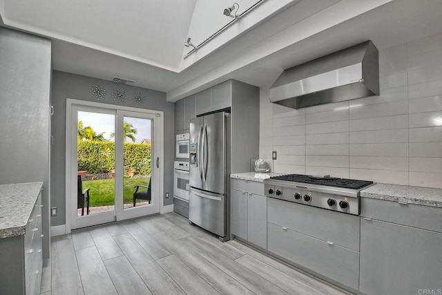 kitchen with decorative backsplash, wall chimney range hood, gray cabinetry, and stainless steel appliances