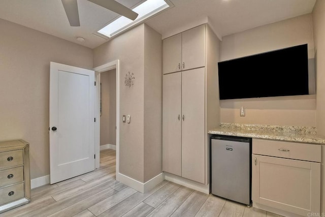 kitchen with light stone counters, light hardwood / wood-style flooring, refrigerator, and ceiling fan