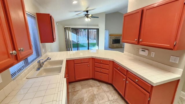 kitchen featuring tile counters, a fireplace, kitchen peninsula, and sink