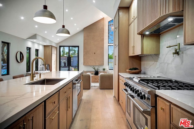 kitchen featuring high end range, light hardwood / wood-style floors, custom range hood, pendant lighting, and sink