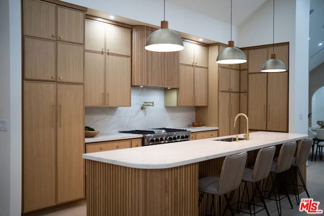 kitchen featuring decorative backsplash, a kitchen island with sink, hanging light fixtures, and sink