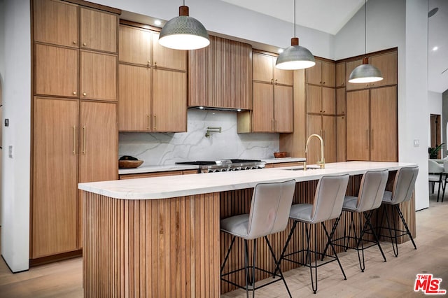 kitchen with tasteful backsplash, pendant lighting, light hardwood / wood-style floors, a center island with sink, and sink