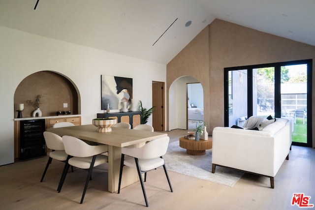 dining space with high vaulted ceiling, beverage cooler, and light wood-type flooring