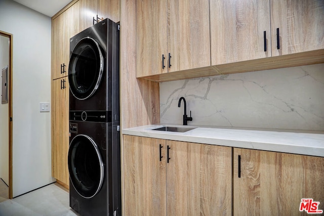 clothes washing area with cabinets, stacked washer / dryer, and sink