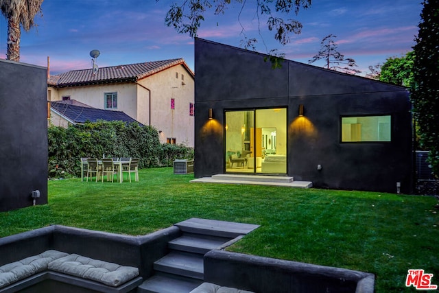 back house at dusk featuring a yard