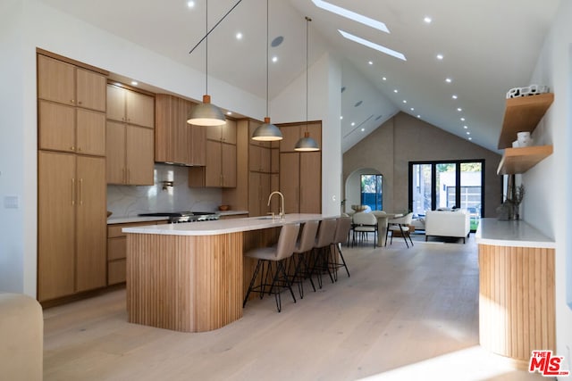 kitchen with a skylight, backsplash, a kitchen breakfast bar, hanging light fixtures, and light hardwood / wood-style flooring