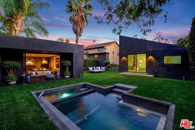 back house at dusk featuring a swimming pool with hot tub, a yard, outdoor lounge area, and a patio