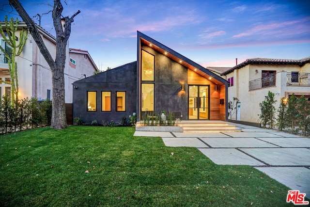 back house at dusk featuring a lawn and a patio area