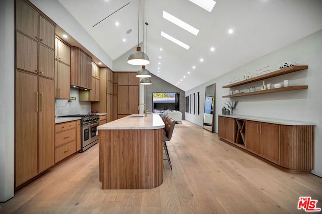 kitchen featuring double oven range, a center island with sink, decorative light fixtures, vaulted ceiling with skylight, and sink