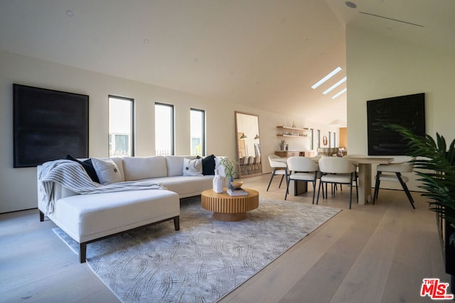 living room featuring a skylight, light hardwood / wood-style flooring, and high vaulted ceiling