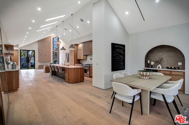 dining area with light hardwood / wood-style floors, sink, high vaulted ceiling, and a skylight