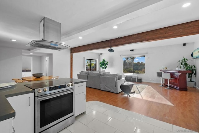 kitchen with stainless steel range with electric cooktop, island exhaust hood, beam ceiling, light hardwood / wood-style floors, and white cabinets