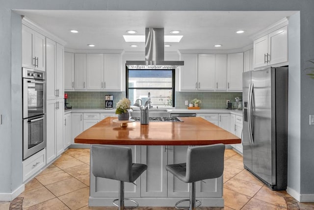 kitchen with appliances with stainless steel finishes, a breakfast bar, white cabinets, island exhaust hood, and a center island