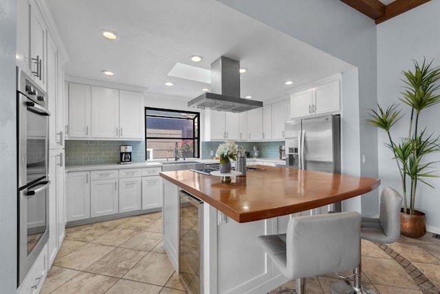 kitchen featuring butcher block countertops, white cabinetry, stainless steel appliances, island exhaust hood, and beverage cooler