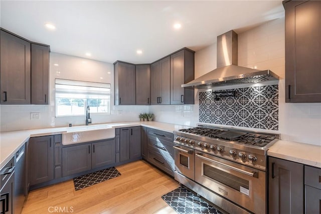 kitchen featuring sink, black dishwasher, light wood-type flooring, range with two ovens, and wall chimney exhaust hood