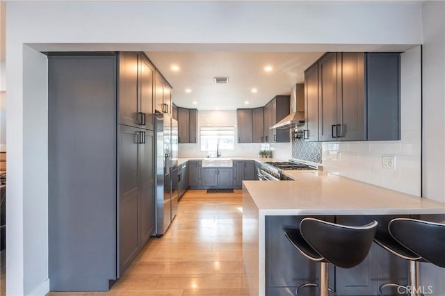 kitchen featuring wall chimney range hood, a breakfast bar, kitchen peninsula, sink, and stainless steel fridge with ice dispenser