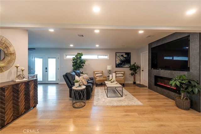 living room featuring french doors, a tiled fireplace, and light hardwood / wood-style floors