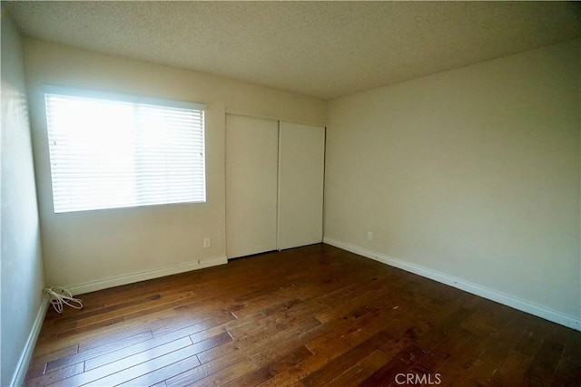 unfurnished bedroom featuring a closet, dark wood-type flooring, multiple windows, and a textured ceiling