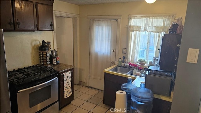 kitchen with sink, light tile patterned floors, stainless steel gas range, and dark brown cabinetry