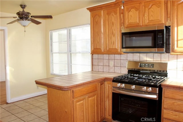 kitchen with light tile patterned floors, appliances with stainless steel finishes, kitchen peninsula, and tile countertops