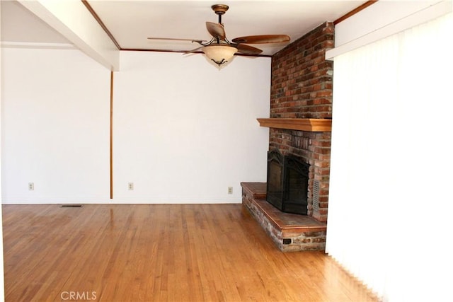 unfurnished living room featuring ceiling fan, hardwood / wood-style floors, ornamental molding, and a fireplace