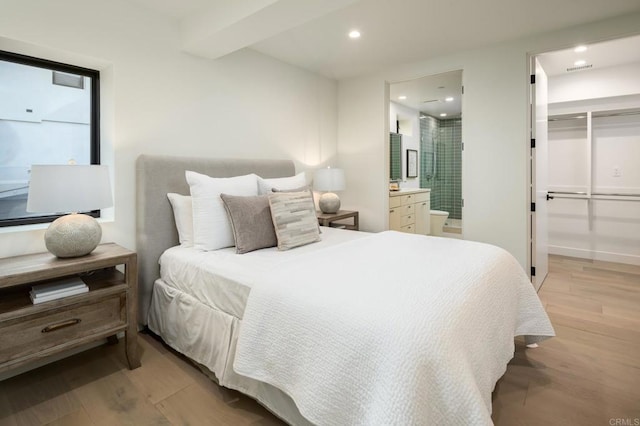 bedroom featuring a spacious closet, light hardwood / wood-style floors, connected bathroom, a closet, and beam ceiling