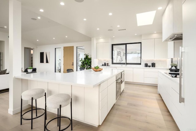 kitchen featuring backsplash, wall chimney range hood, white cabinetry, a kitchen breakfast bar, and a large island