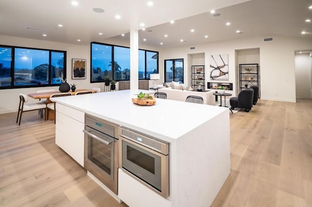 kitchen with oven, light hardwood / wood-style floors, white cabinetry, and a center island