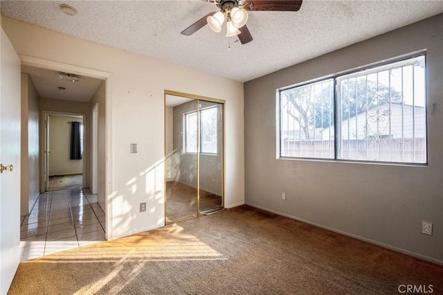 unfurnished bedroom with a textured ceiling, a closet, light colored carpet, and ceiling fan