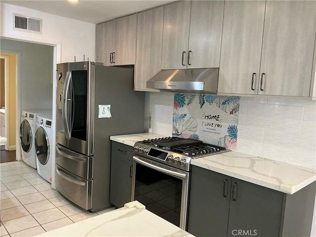 kitchen with gray cabinetry, light stone counters, stainless steel appliances, washer and clothes dryer, and backsplash